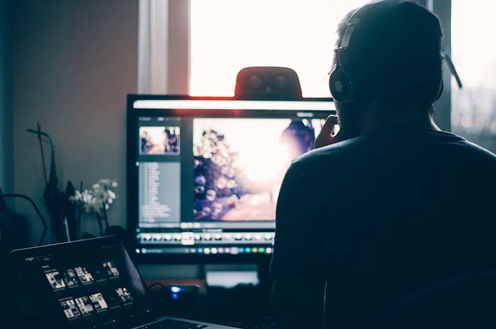 chico de espaldas a la cámara y de frente a un ordenador con un programa de producción de video abierto y unos auriculares puestos. 