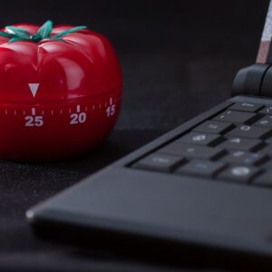 Técnica pomodoro. En la imagen aparece un cronómetro de cocina con forma de tomate junto a un ordenador.  